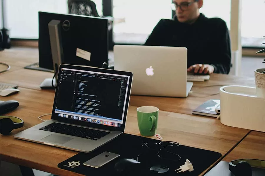 Managed IT solutions blog image of man sitting at a table with cmuter running a script Photo by Djordje Petrovic: https://www.pexels.com/photo/man-in-black-shirt-sits-behind-desk-with-computers-2102416/