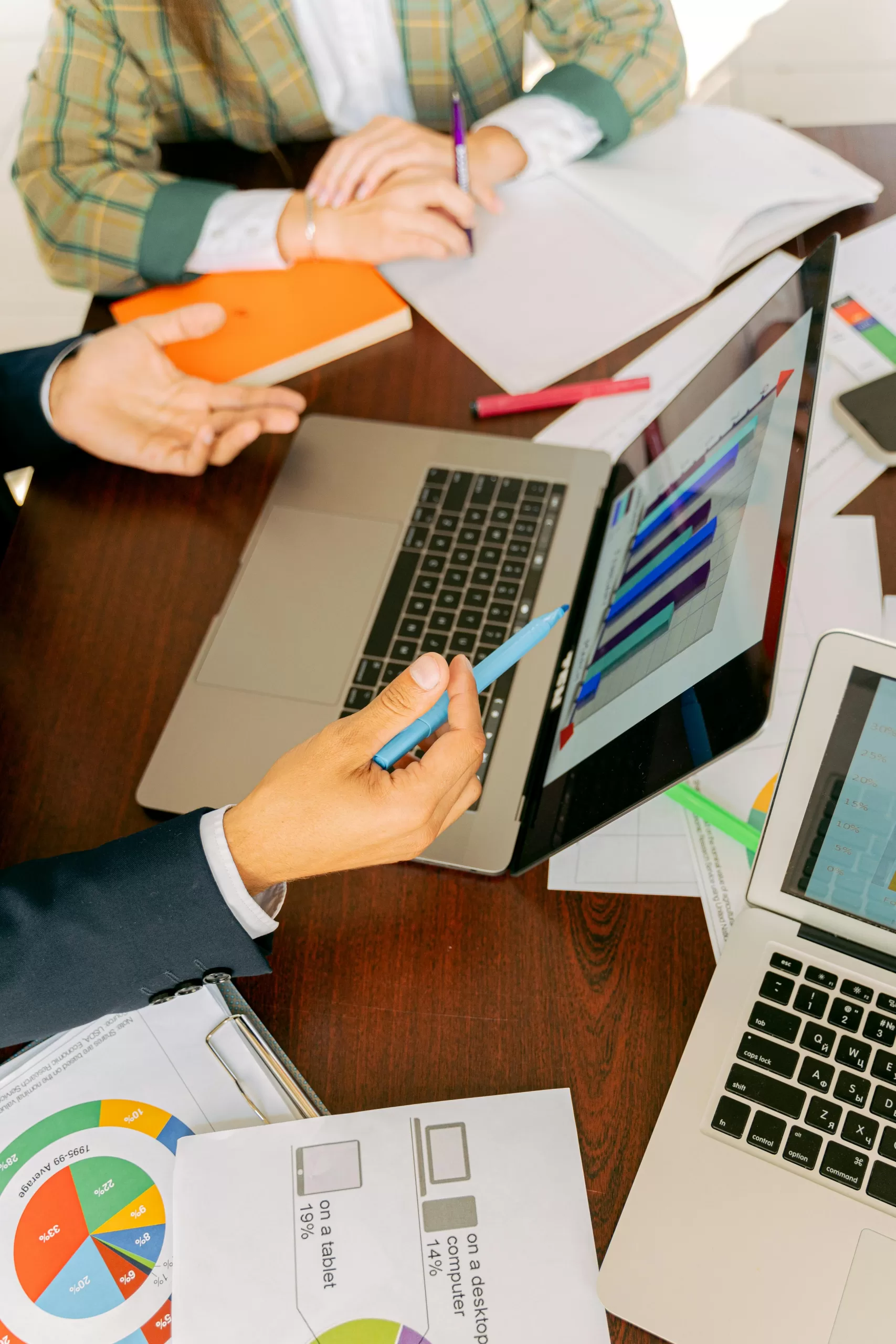 Close up of a laptop screen with a bar chart and hands gesticulating whilst holding a pen. - Data Lifecycle management Blog