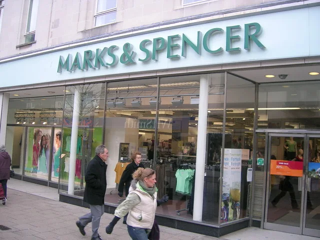 Shoppers walking past a Marks & Spencer storefront on a UK high street.