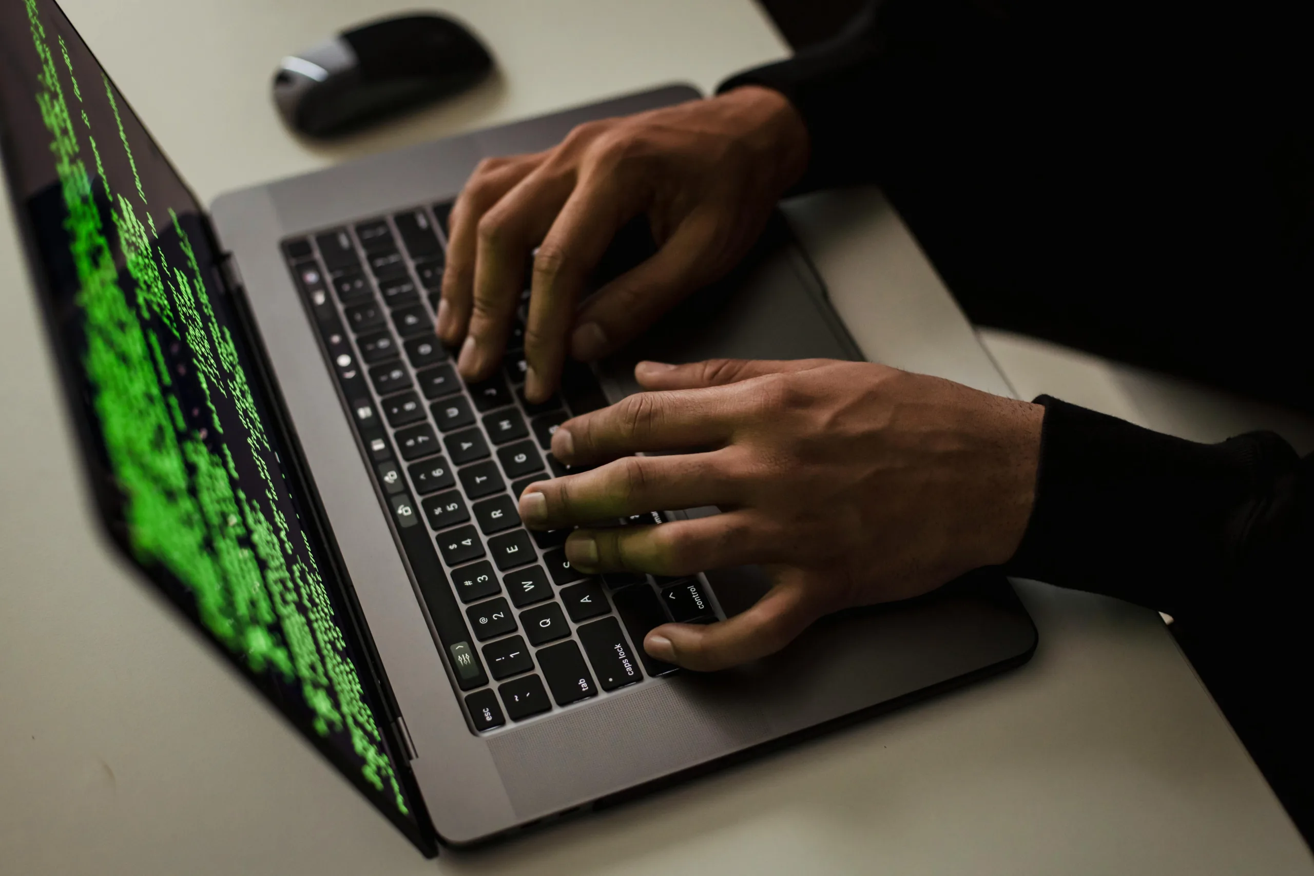 Close-up of hands typing on a laptop displaying green code, suggesting cybersecurity activity or system monitoring.