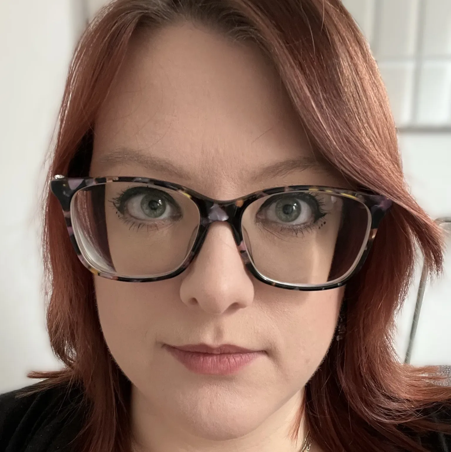Elle Borland close-up headshot wearing glasses, with red hair and a confident expression, against a softly blurred background.