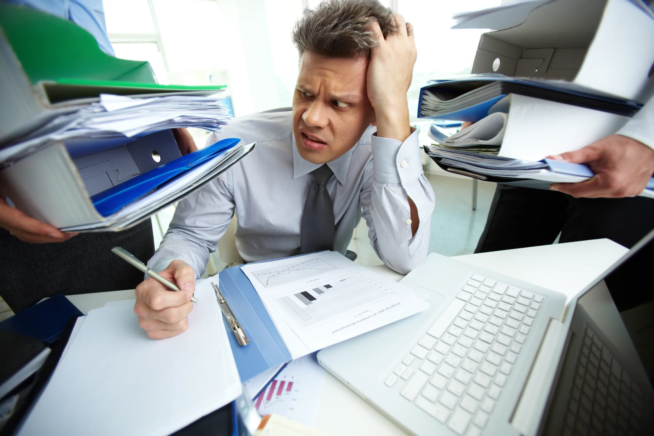 Stressed businessman surrounded by stacks of paperwork and files, representing data overload in business.