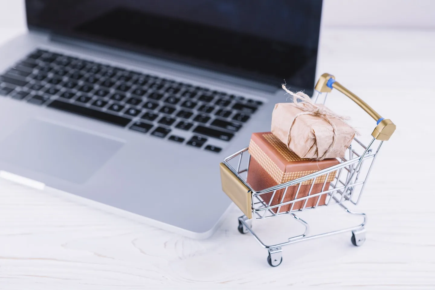 Mini shopping cart with gift boxes beside a laptop, representing secure online holiday shopping with password managers and virtual cards.
