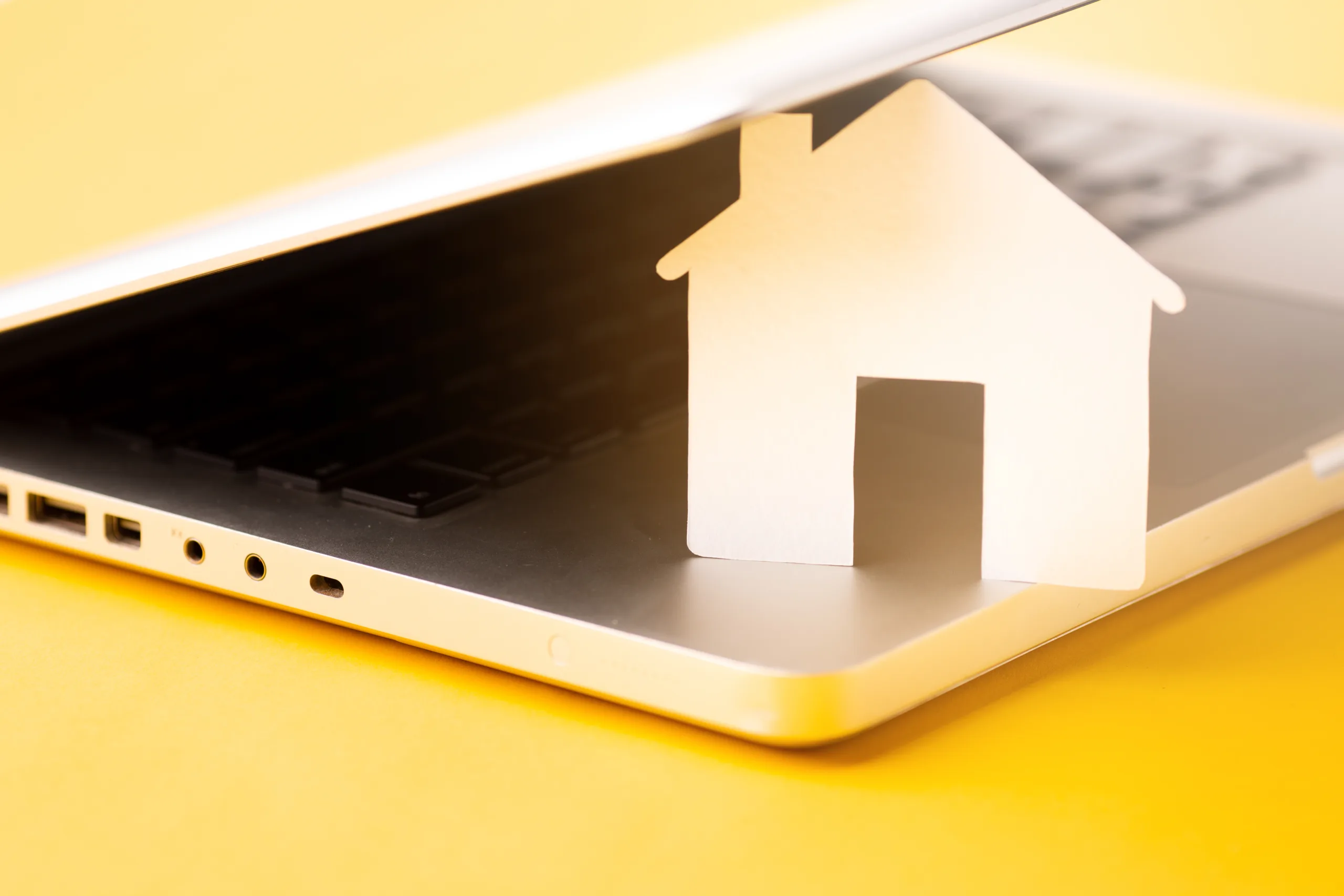 A paper house model sitting on a laptop, representing home cybersecurity, secure home networks, and smart device protection.
