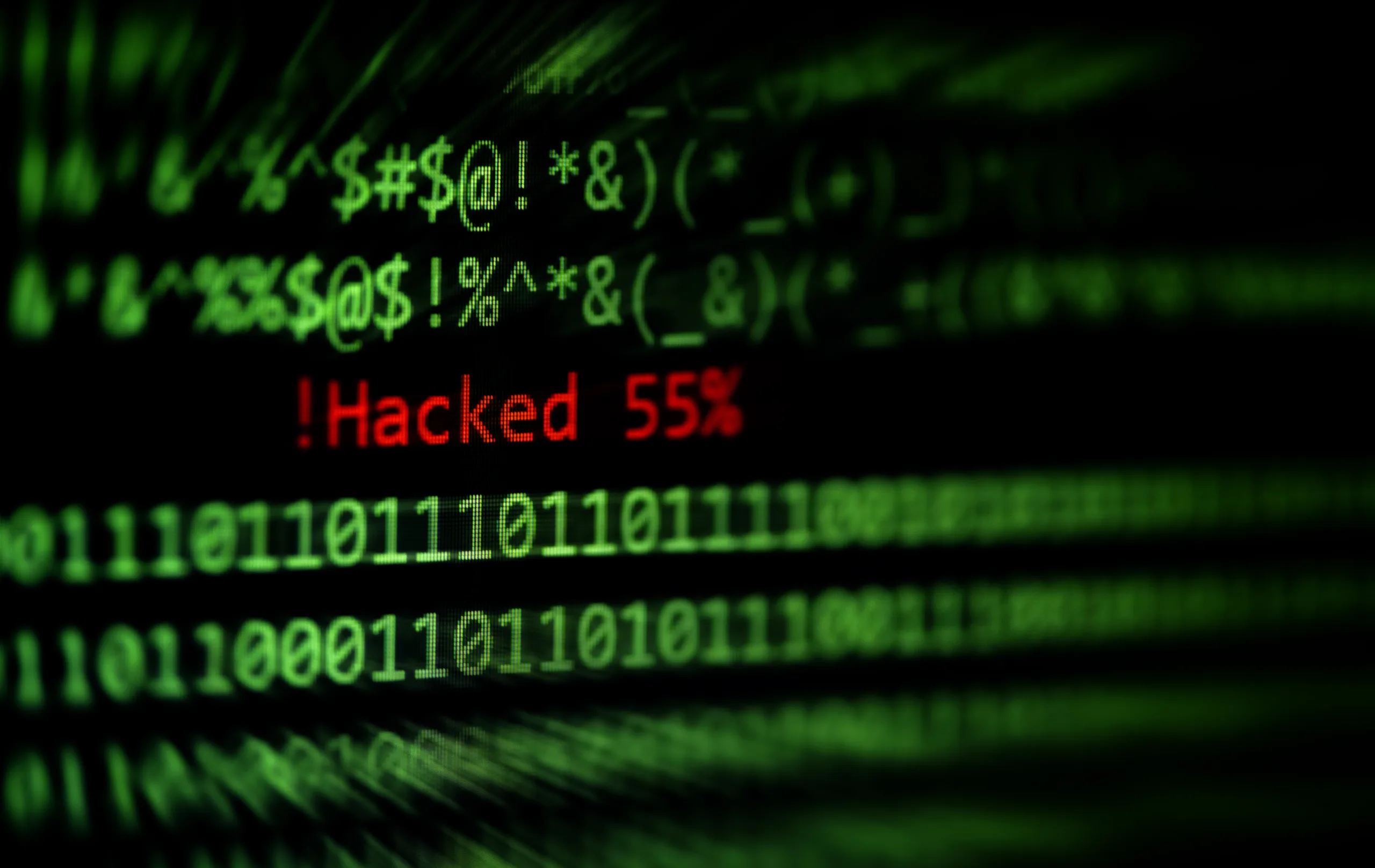 A computer screen showing green code and a red hacked warning message, representing a compromised PC or cyberattack.