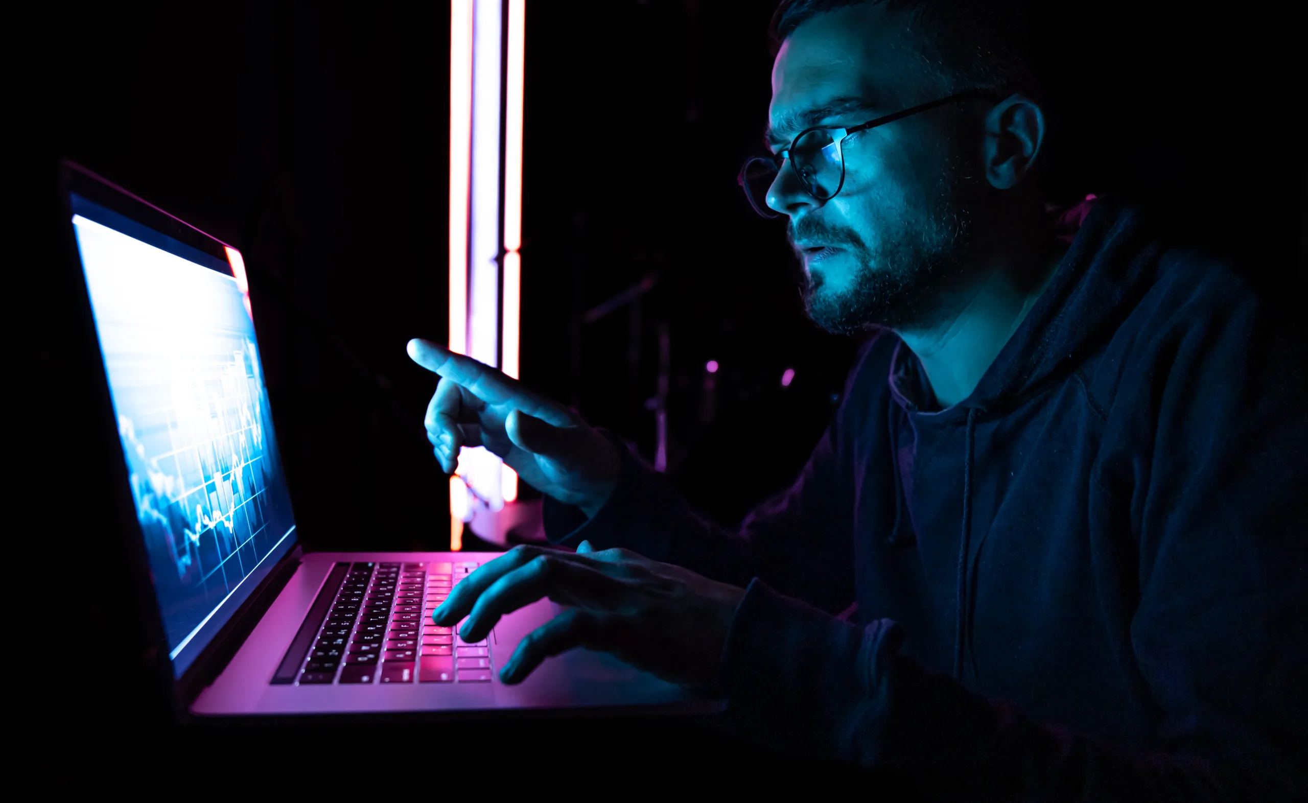 A person analysing data on a laptop in a dark setting, representing cybersecurity monitoring and online threat detection.