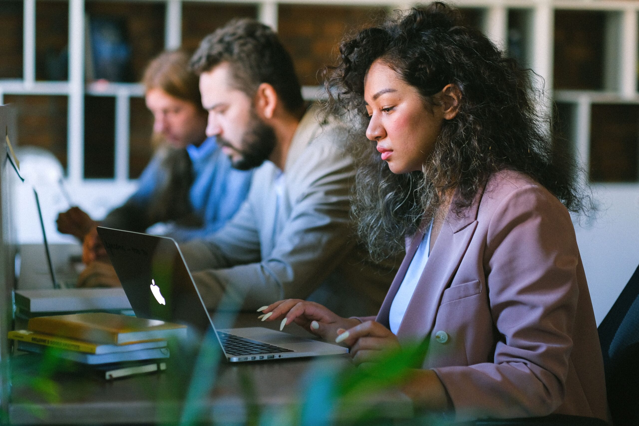 Three colleagues sitting in a row at a shared office desk working on their laptops.